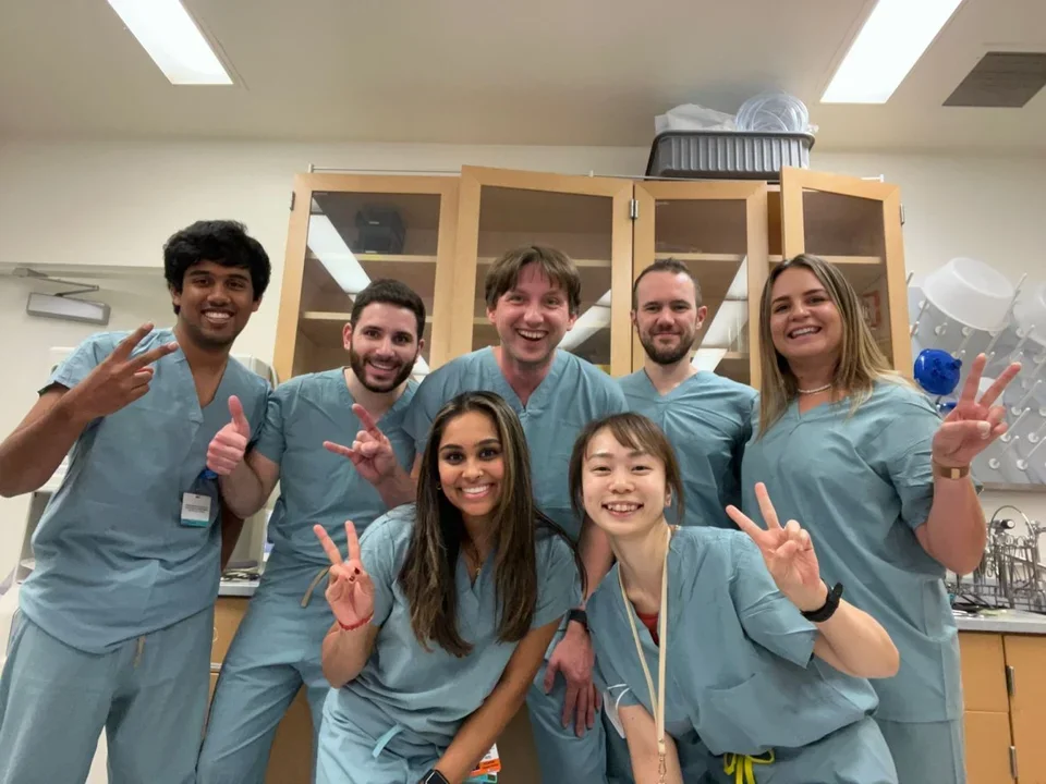 Ajijola Lab members in light blue scrubs smiling and posing with peace signs in a lab setting.